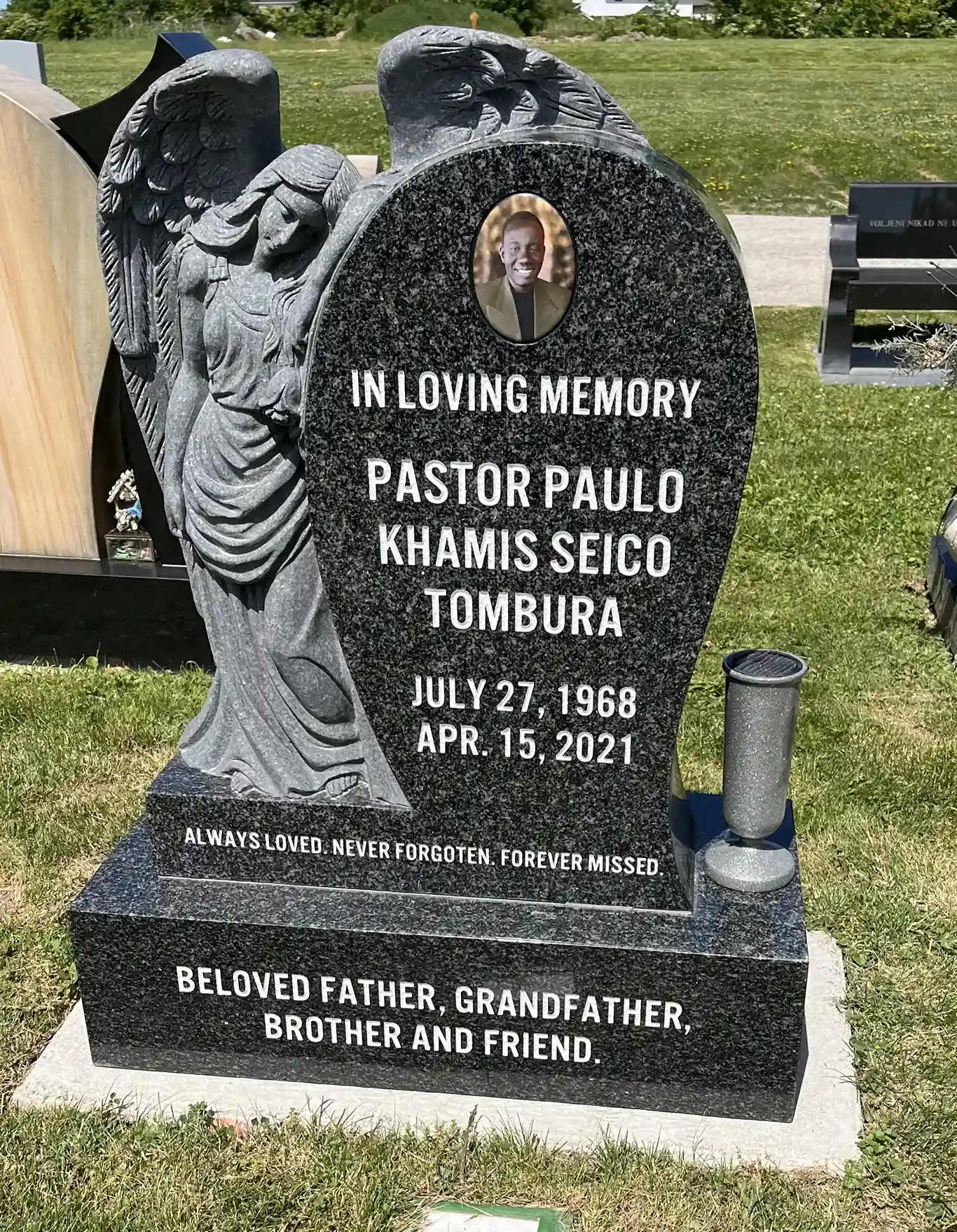 Black headstone with angel statue next to headstone.